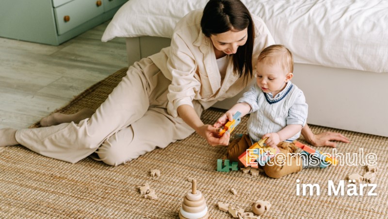 Mutter und Kleinkind spielen auf einem Teppich mit Holzspielzeug.